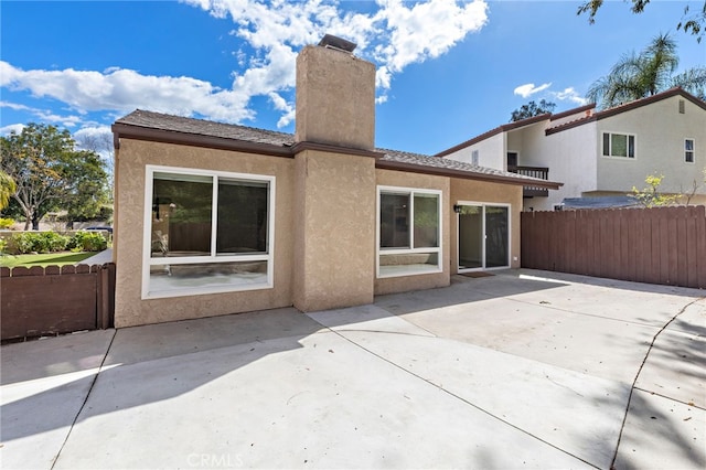 rear view of property featuring stucco siding, a chimney, fence, and a patio