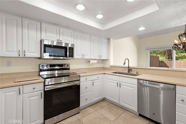 kitchen featuring white cabinets, a tray ceiling, stainless steel appliances, and a sink