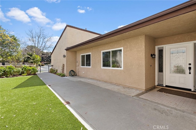 exterior space with a gate, a patio area, a yard, and stucco siding