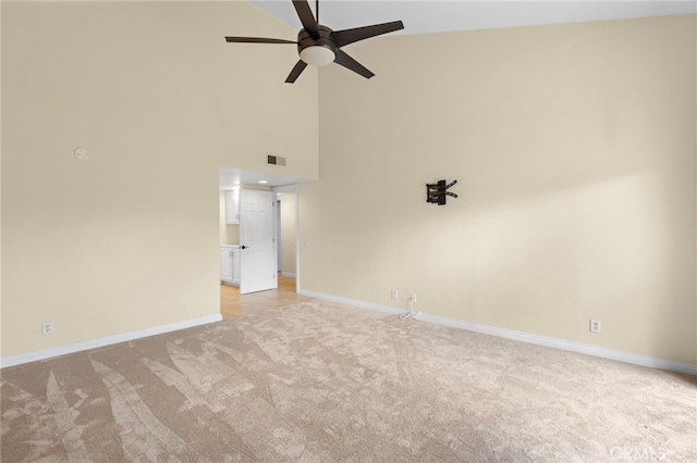 empty room with ceiling fan, light colored carpet, visible vents, baseboards, and a towering ceiling