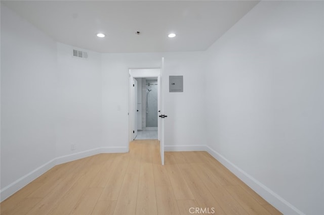 spare room featuring light wood finished floors, baseboards, electric panel, and visible vents