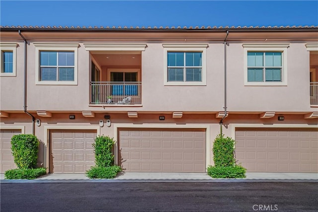 view of property featuring a garage, a balcony, and stucco siding