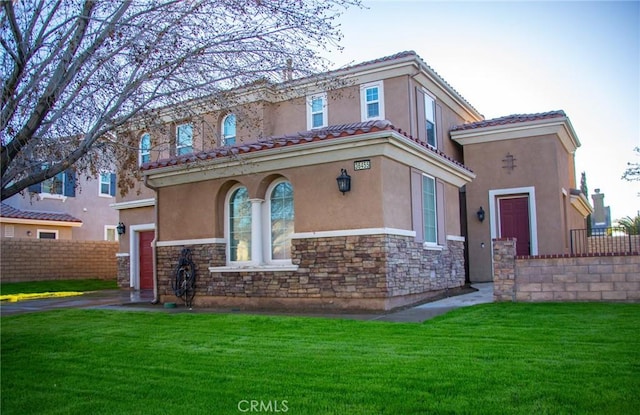 mediterranean / spanish home featuring stone siding, fence, a front lawn, and stucco siding