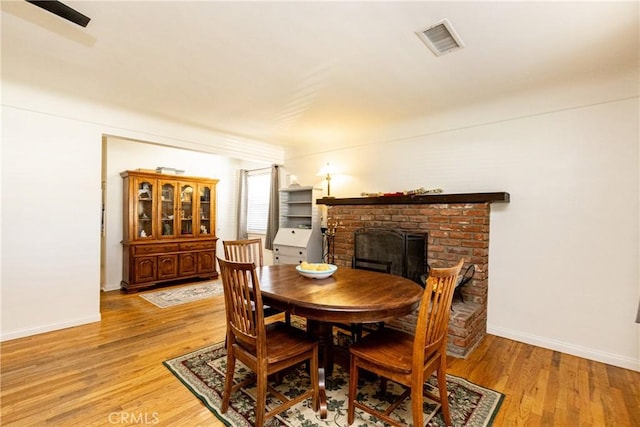 dining room featuring light wood-style floors, visible vents, a fireplace, and baseboards