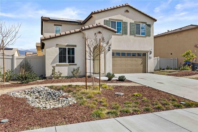 mediterranean / spanish-style house with concrete driveway, an attached garage, fence, roof mounted solar panels, and stucco siding