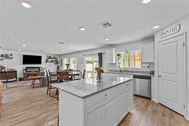 kitchen featuring light wood finished floors, visible vents, a kitchen island, a sink, and dishwasher