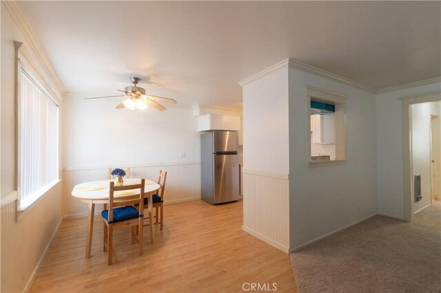 dining room with ornamental molding, a wainscoted wall, light wood finished floors, and a ceiling fan