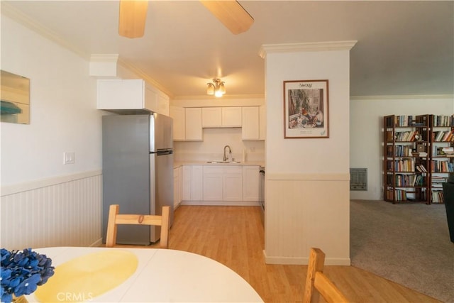 kitchen featuring a sink, white cabinets, ornamental molding, wainscoting, and freestanding refrigerator