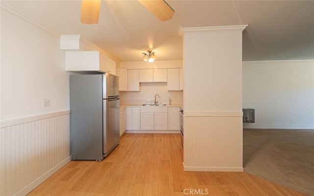 kitchen featuring crown molding, light wood-style flooring, freestanding refrigerator, wainscoting, and a sink