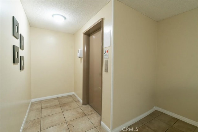 hallway with light tile patterned floors, baseboards, elevator, and a textured ceiling