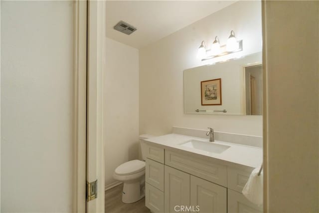 bathroom with toilet, visible vents, wood finished floors, and vanity