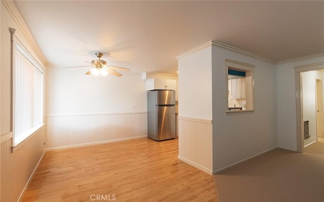 unfurnished room featuring a wainscoted wall, ceiling fan, ornamental molding, and light wood-style flooring