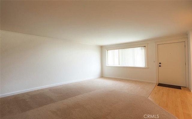 spare room featuring light carpet, crown molding, and baseboards