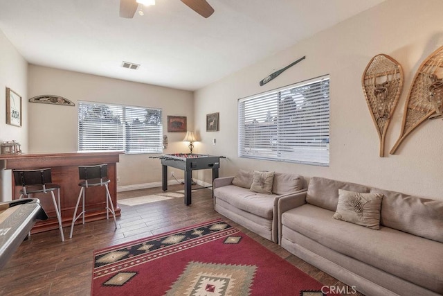 living room featuring ceiling fan, visible vents, baseboards, a dry bar, and dark wood finished floors