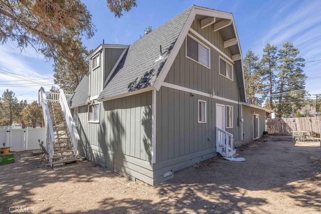 view of property exterior featuring roof with shingles, fence, and stairs