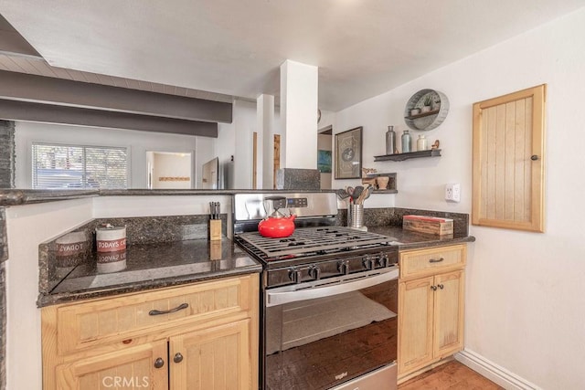 kitchen featuring baseboards, dark stone counters, light brown cabinetry, and gas stove