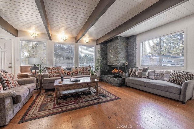 living area with plenty of natural light, a stone fireplace, beamed ceiling, and hardwood / wood-style flooring