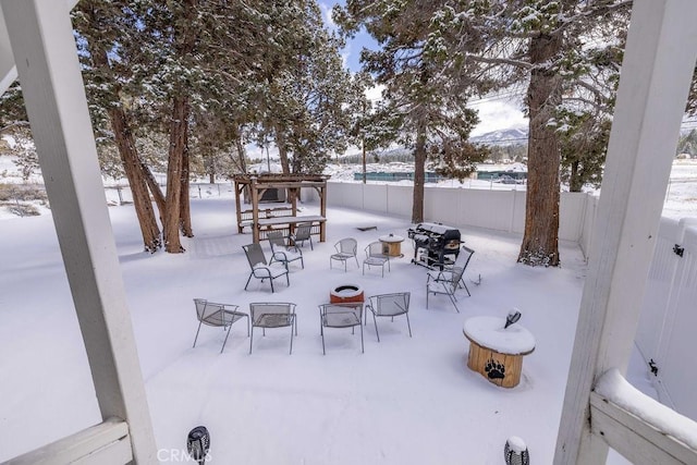 snow covered patio with an outdoor fire pit, grilling area, fence, and a pergola