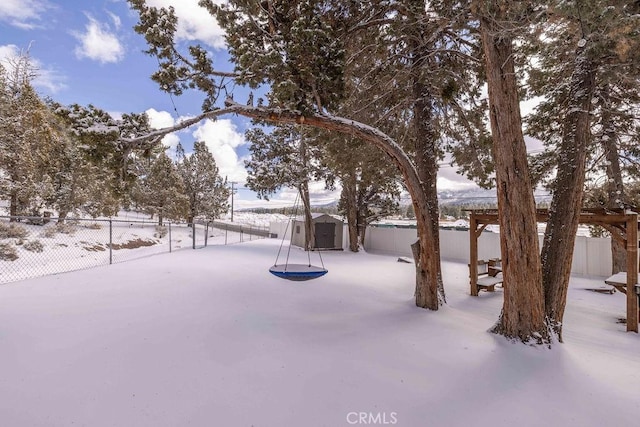 yard covered in snow featuring a storage unit, an outdoor structure, and a fenced backyard