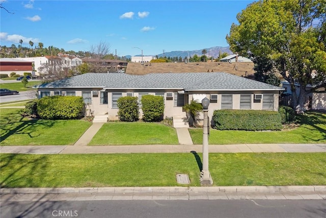 ranch-style house with stucco siding, a shingled roof, a mountain view, and a front yard