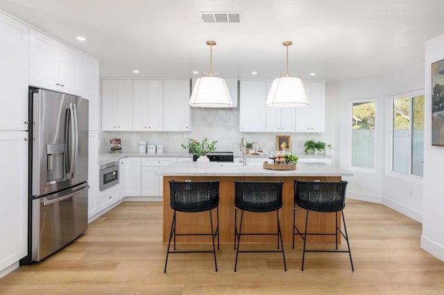 kitchen with visible vents, light wood-style floors, light countertops, backsplash, and stainless steel fridge with ice dispenser