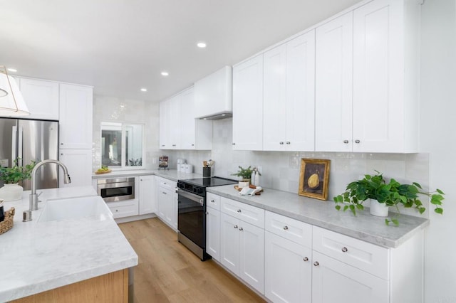 kitchen with a sink, white cabinetry, light wood-style floors, appliances with stainless steel finishes, and backsplash