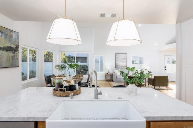 kitchen featuring light stone counters, a sink, visible vents, open floor plan, and hanging light fixtures