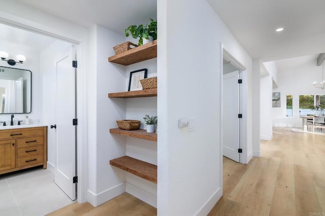 hall with light wood-type flooring, baseboards, a notable chandelier, and a sink