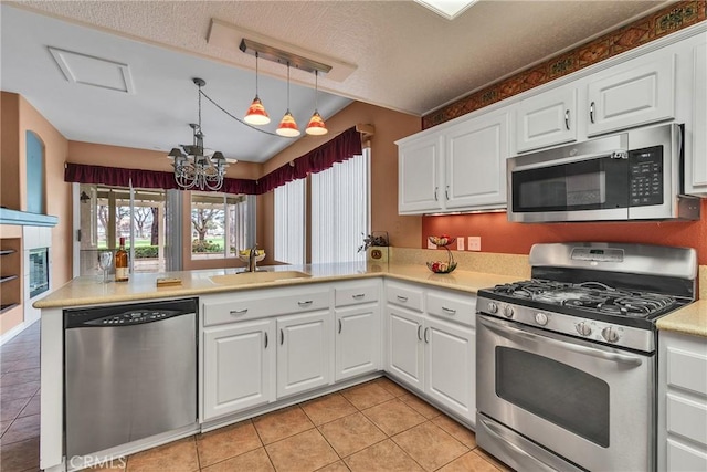 kitchen with a sink, appliances with stainless steel finishes, a peninsula, an inviting chandelier, and light countertops