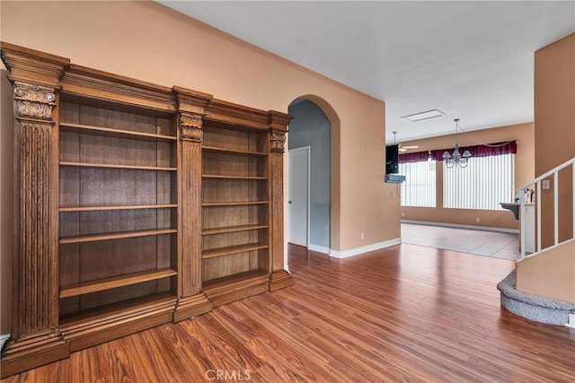 unfurnished living room featuring wood finished floors, arched walkways, a chandelier, and baseboards