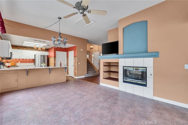 kitchen featuring a tiled fireplace, ceiling fan with notable chandelier, freestanding refrigerator, a peninsula, and light countertops