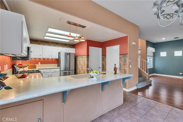 kitchen with a peninsula, light countertops, freestanding refrigerator, and a sink