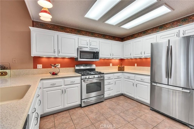 kitchen with a sink, white cabinetry, stainless steel appliances, light tile patterned flooring, and light countertops