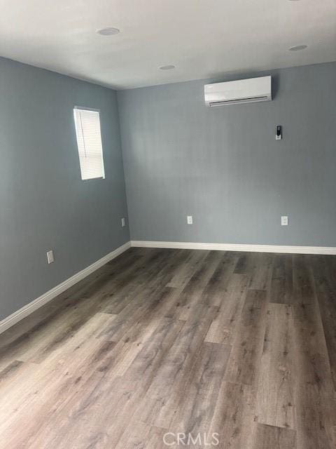 unfurnished room featuring a wall mounted AC, wood finished floors, and baseboards