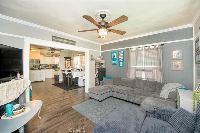 living room with a ceiling fan, ornamental molding, and dark wood-style flooring