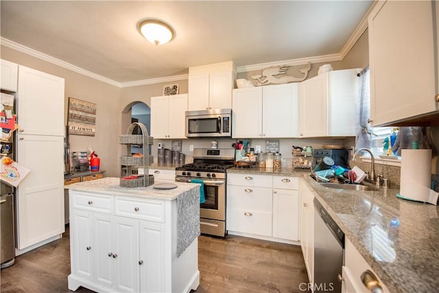 kitchen with appliances with stainless steel finishes, ornamental molding, white cabinetry, a sink, and wood finished floors