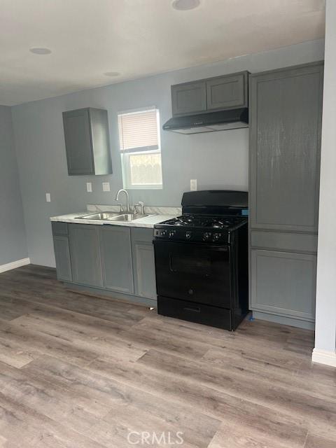 kitchen featuring black range with gas stovetop, gray cabinets, light wood-type flooring, under cabinet range hood, and a sink