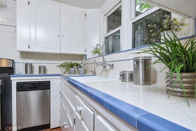 kitchen featuring tile countertops, a sink, white cabinets, appliances with stainless steel finishes, and tasteful backsplash