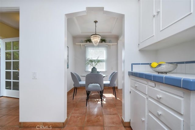 dining area featuring light tile patterned floors, a raised ceiling, and a notable chandelier