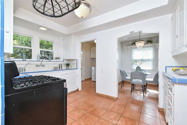 kitchen with decorative backsplash, a raised ceiling, black gas stove, white cabinetry, and a notable chandelier