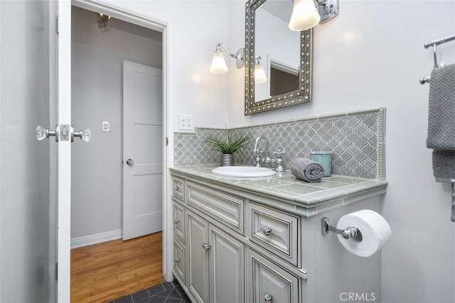 bathroom with baseboards, backsplash, vanity, and wood finished floors