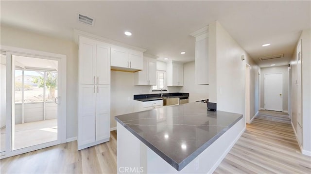 kitchen featuring light wood finished floors, dark countertops, visible vents, white cabinets, and a sink