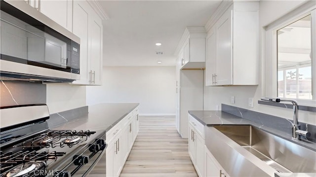 kitchen featuring appliances with stainless steel finishes, white cabinets, a sink, and dark stone counters