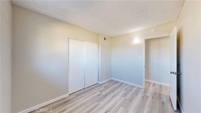 unfurnished bedroom featuring a textured ceiling, a closet, wood finished floors, and baseboards