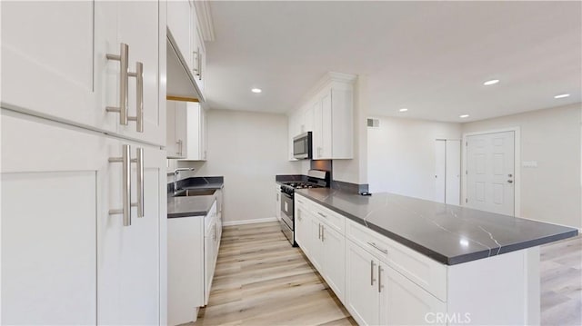 kitchen with dark countertops, a peninsula, appliances with stainless steel finishes, and a sink