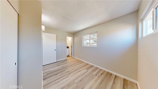 empty room with light wood-style floors, a textured ceiling, and baseboards