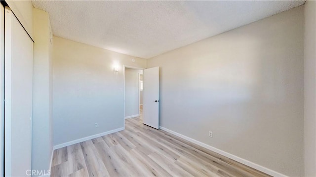 unfurnished room featuring light wood-type flooring, a textured ceiling, and baseboards