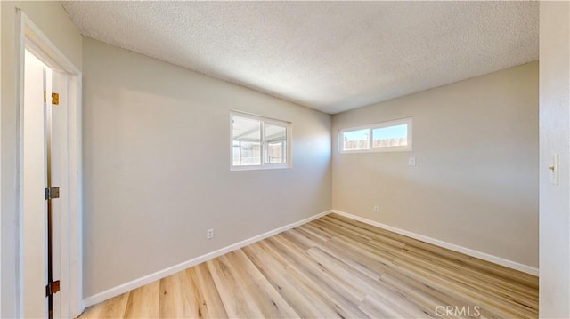 spare room featuring light wood-type flooring, a textured ceiling, and baseboards