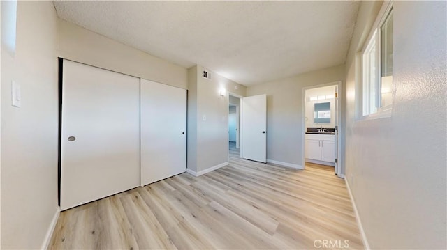 unfurnished bedroom with a sink, visible vents, baseboards, a closet, and light wood-type flooring