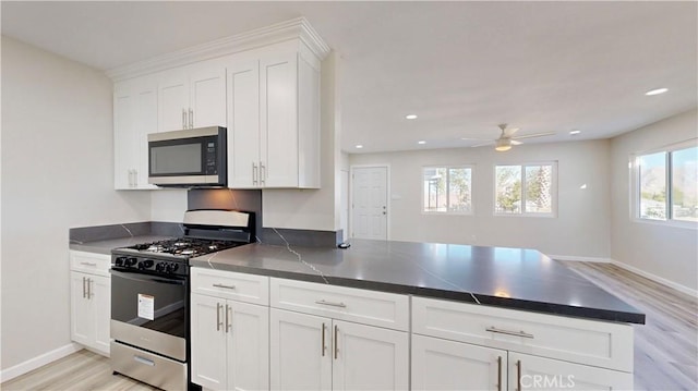 kitchen with stainless steel microwave, a peninsula, white cabinets, gas range oven, and dark countertops